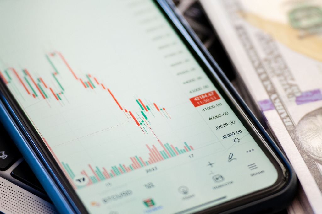 Smartphone displaying sharp price drop candlestick chart with currency and financial metrics